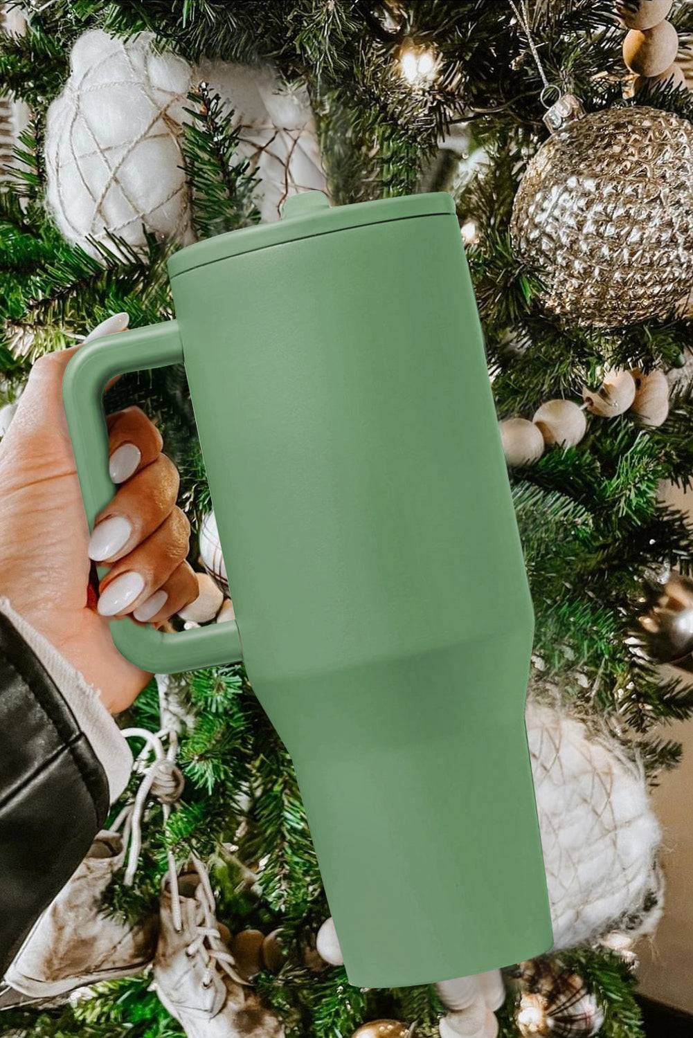 Green tumbler held in front of a decorated Christmas tree