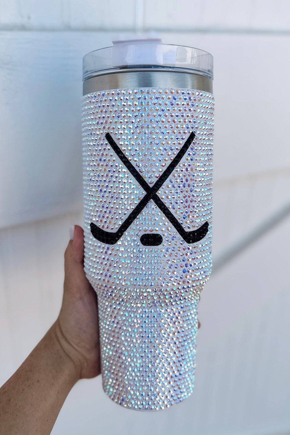 Silver blinged-out tumbler with hockey stick and puck design held by a hand against a white background