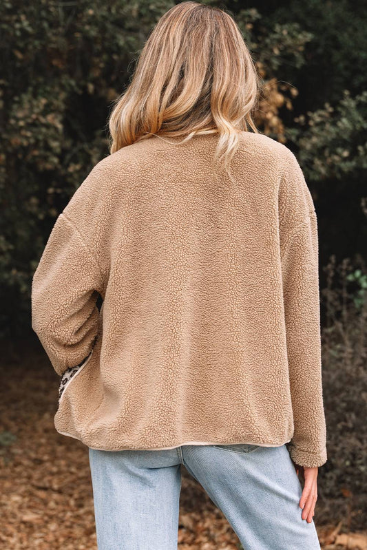 Person wearing a beige fleece jacket and light blue jeans standing outdoors with trees in the background.