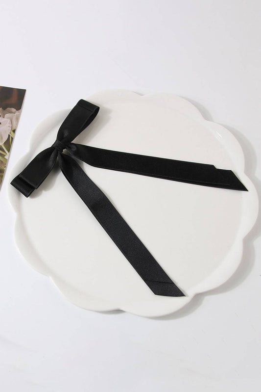 White scalloped-edge plate with a black ribbon on a white background