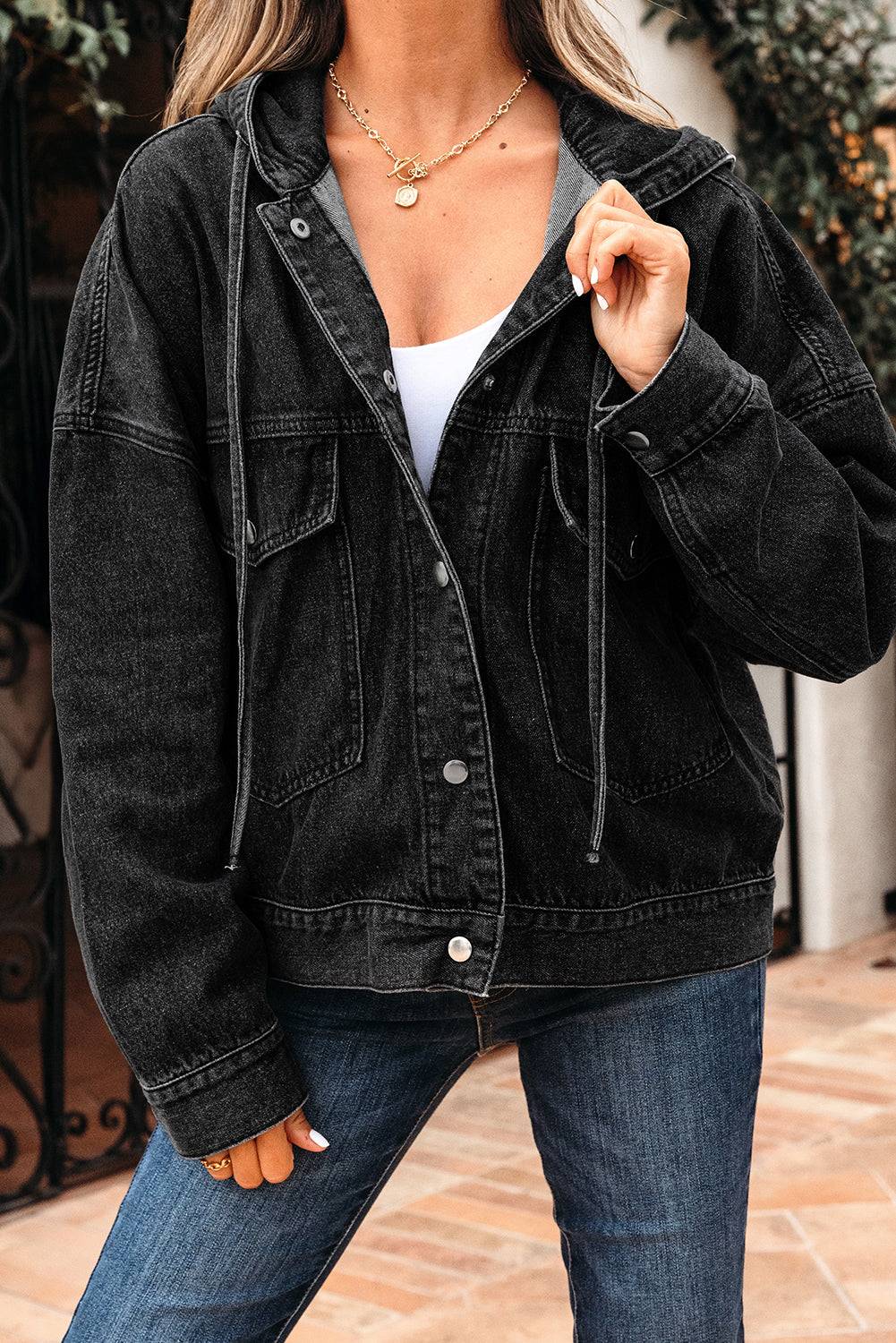 Person wearing a black denim jacket and blue jeans outdoors.