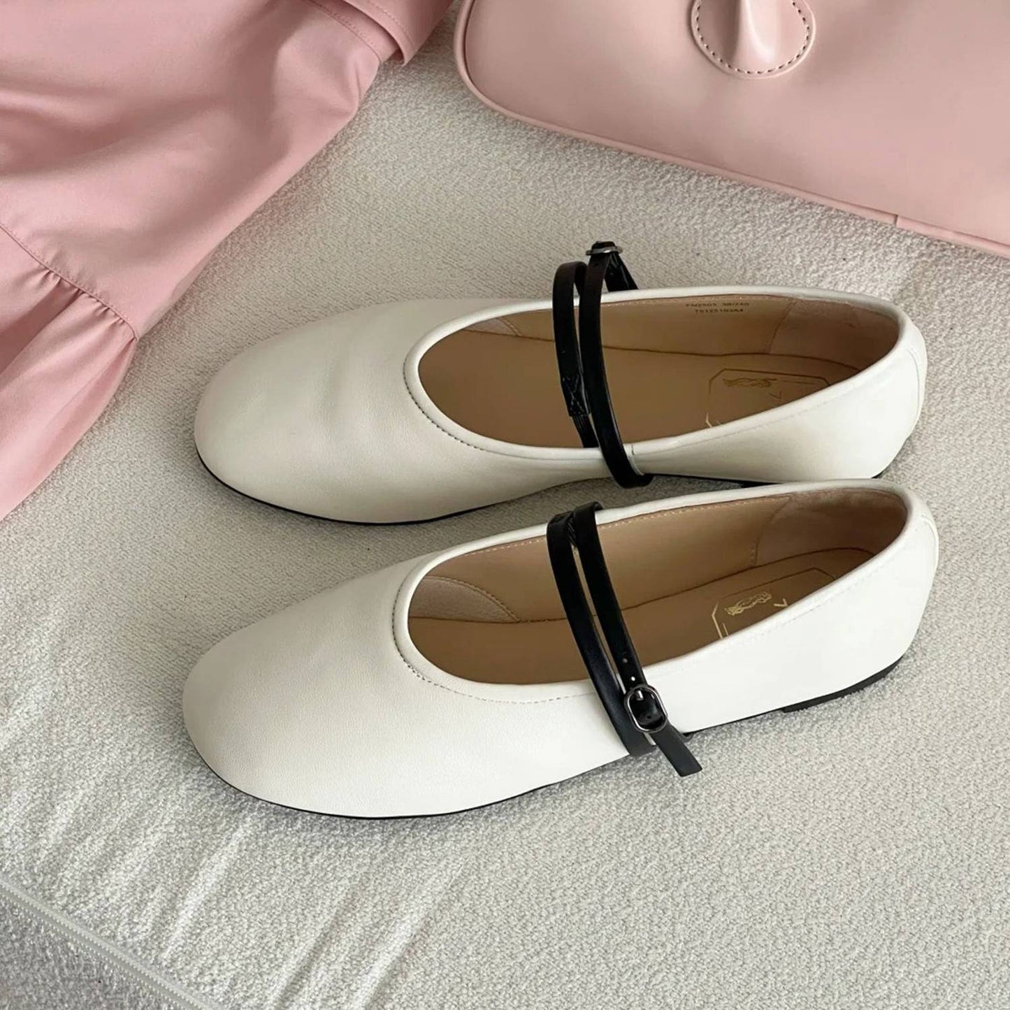 White shoes with black straps on a textured surface with a pink garment in the background