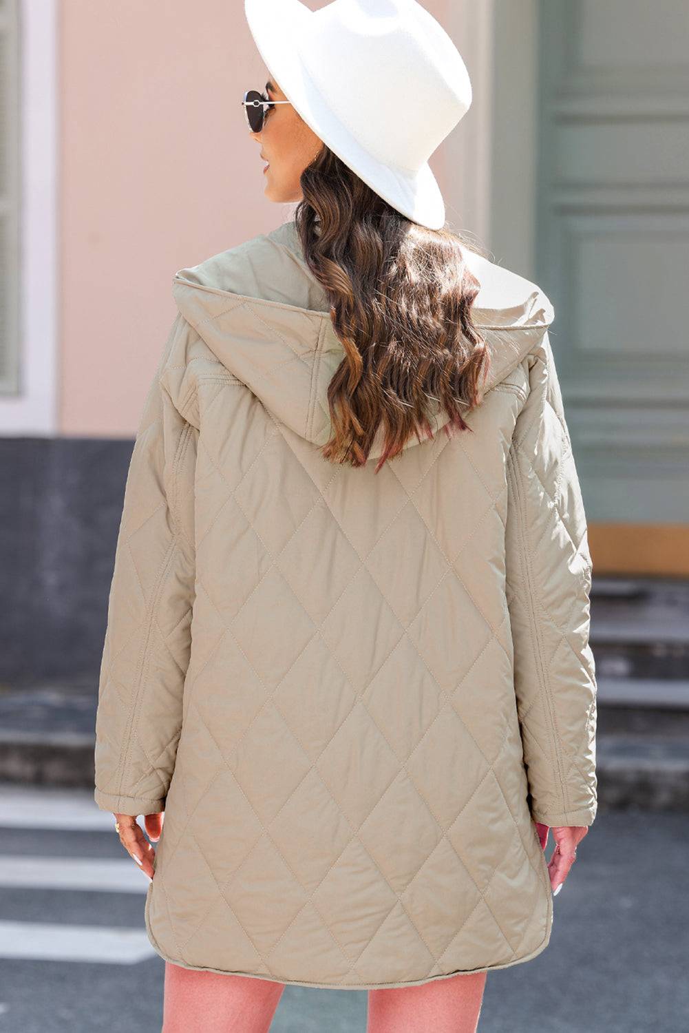Woman wearing a beige quilted coat and white hat on a street.