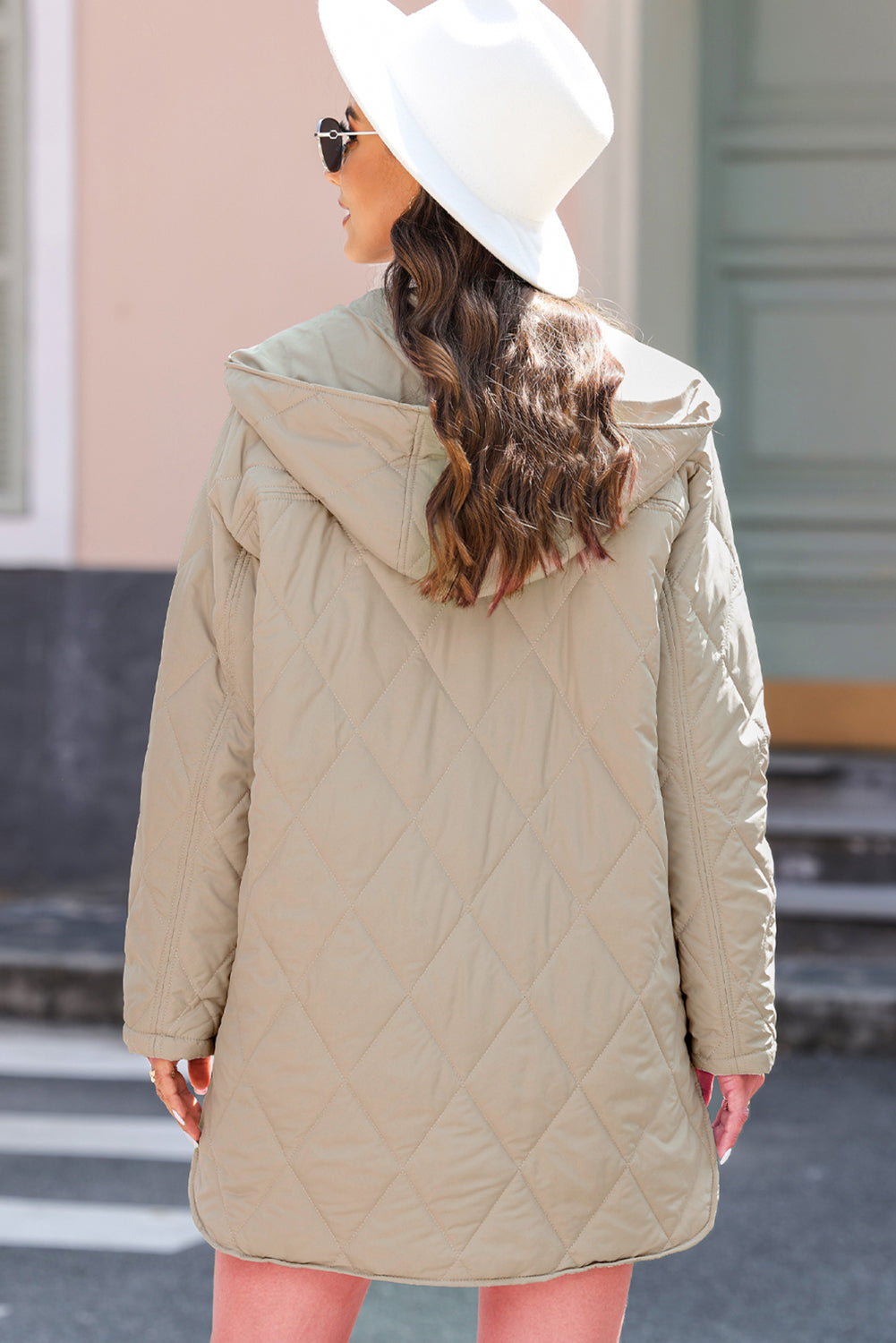 Woman wearing a beige quilted coat and white hat on a street.