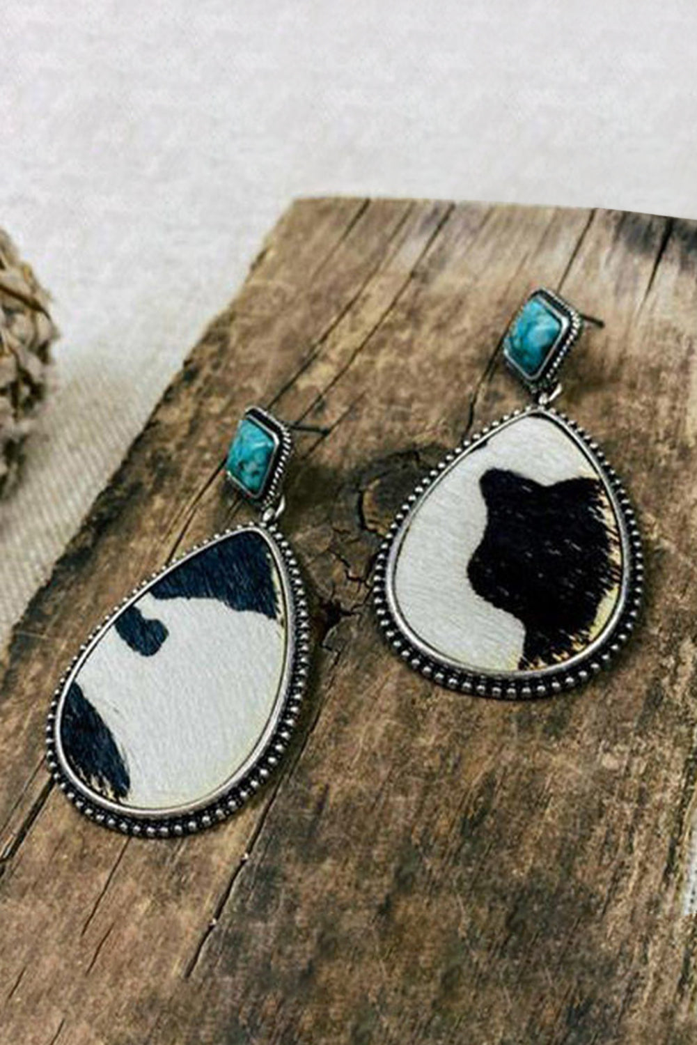 Teardrop-shaped earrings with black, white, and turquoise design on a wooden surface.