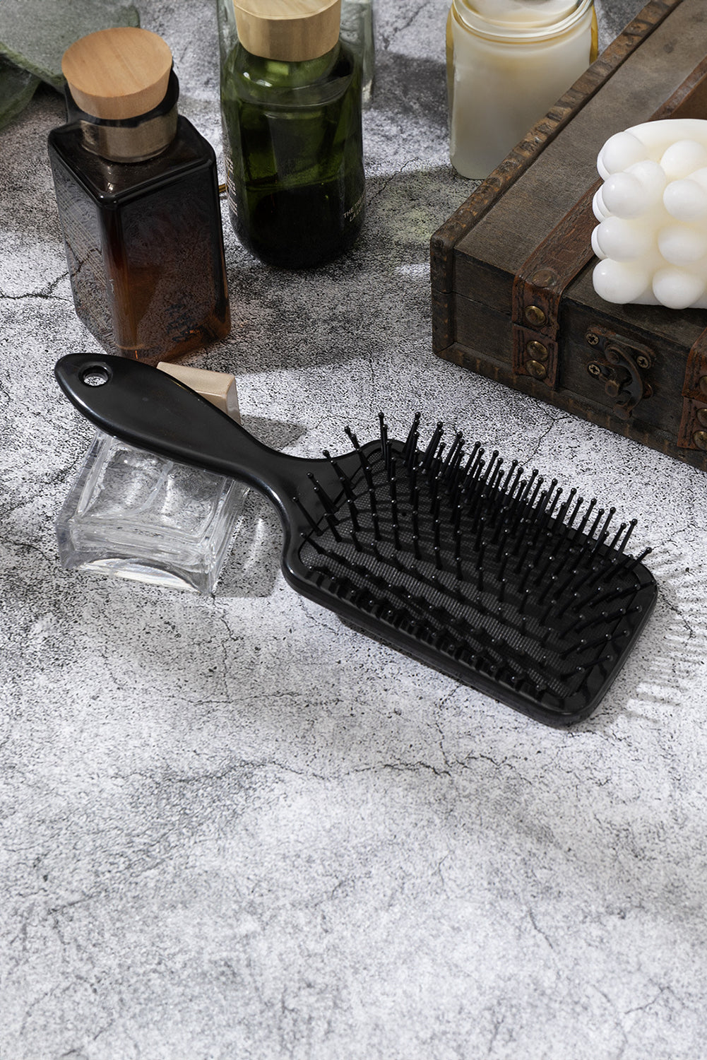 Black hairbrush on a textured surface with bottles and candles in the background