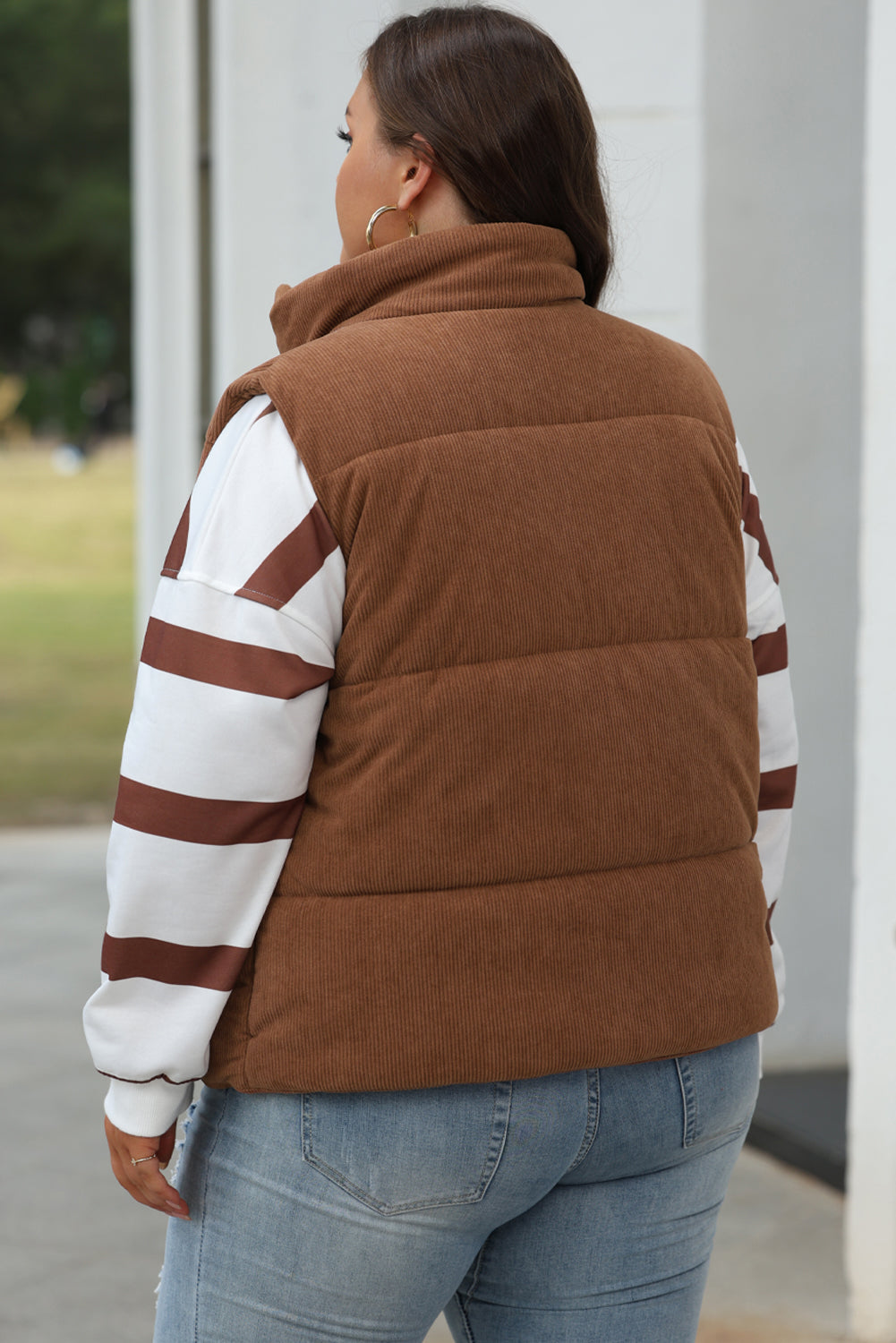 Person wearing a brown puffer vest over a striped shirt with a blurred background