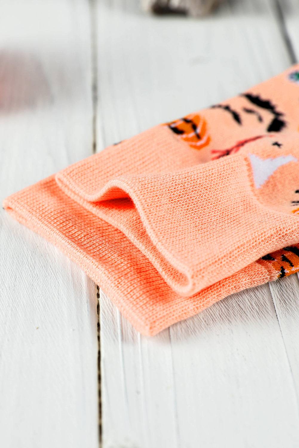 Pair of peach-colored socks with black cat designs on a light wooden surface
