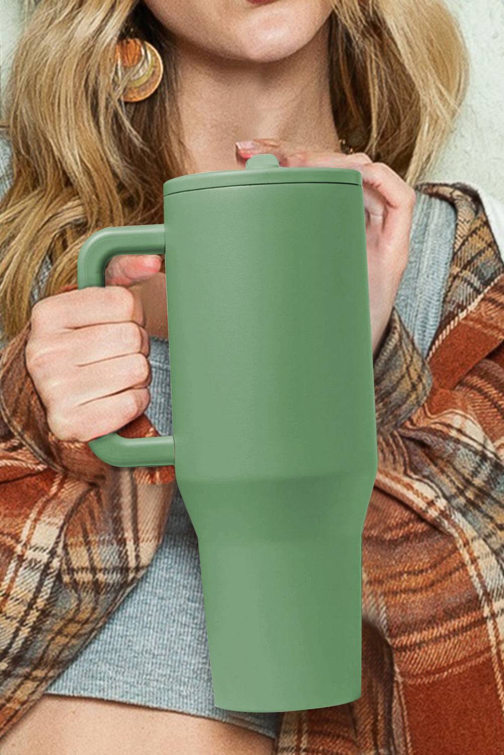 Person holding a green travel mug with a plaid scarf