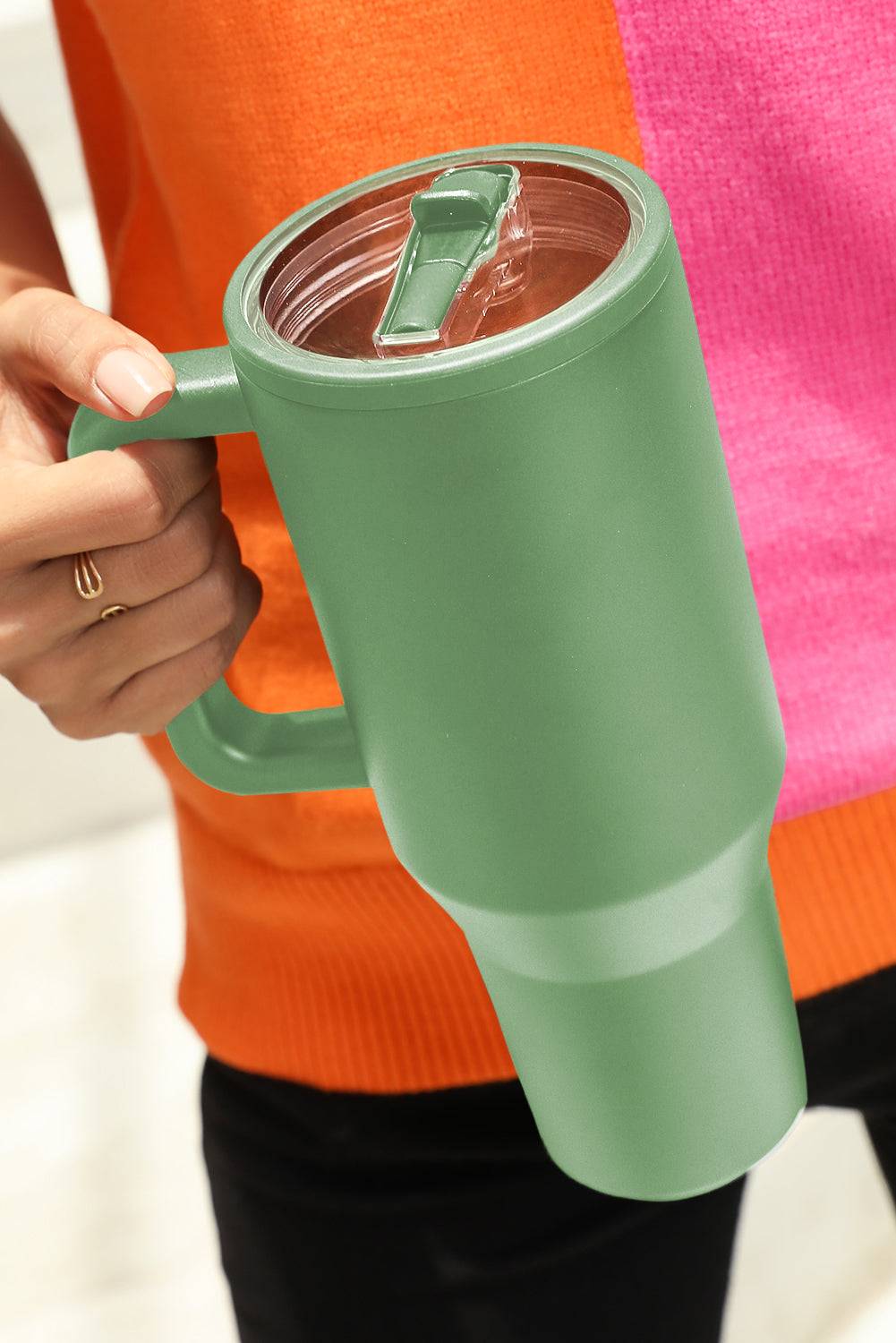 Green mug with a clear lid held by a person wearing an orange sweater.