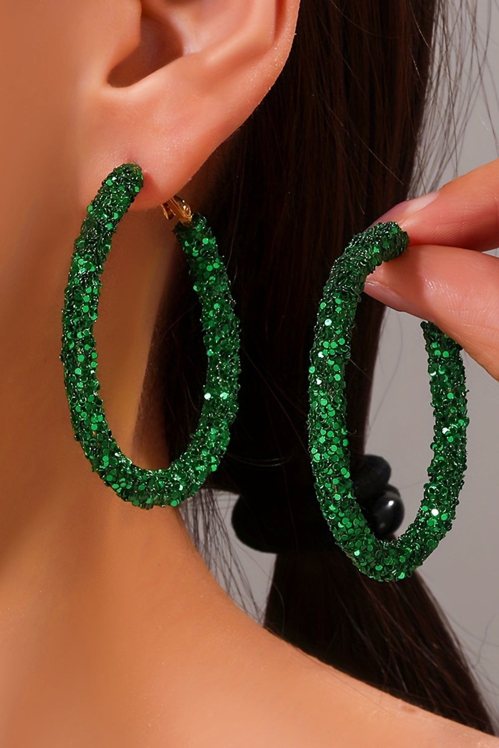 Green glittery hoop earrings being worn on a model's ear.