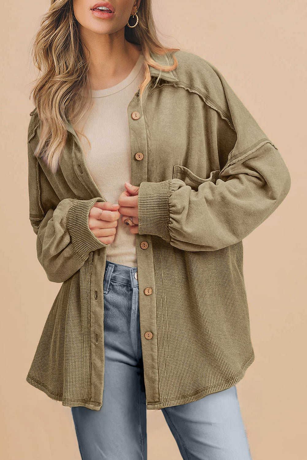 Woman wearing a green jacket over a white shirt and blue jeans on a beige background