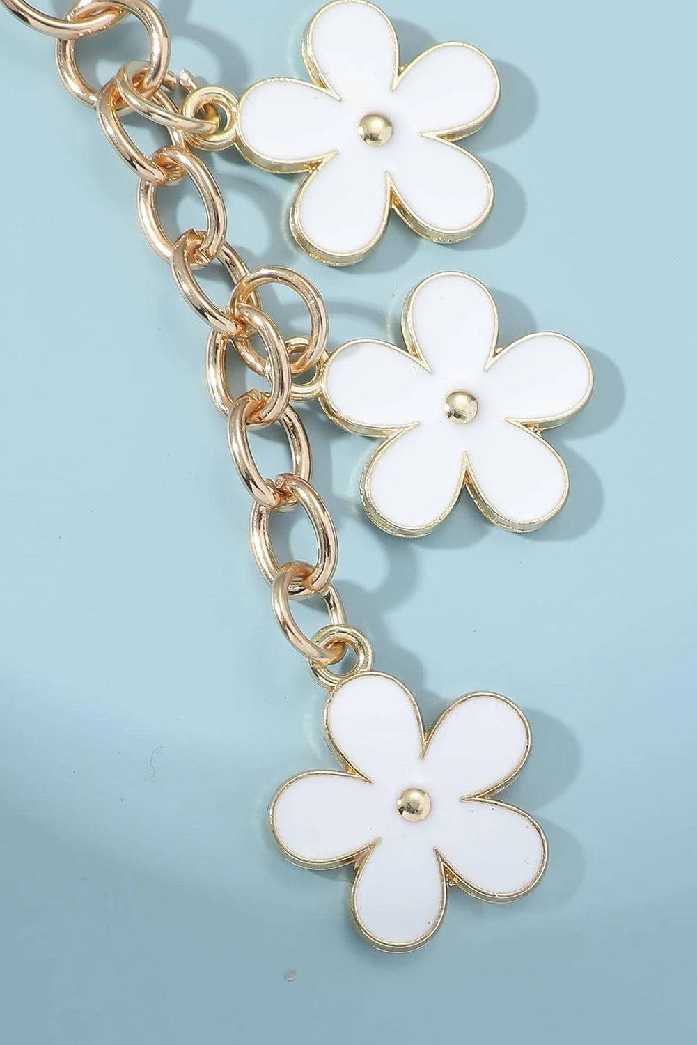 Gold chain bracelet with white flower charms on a light blue background