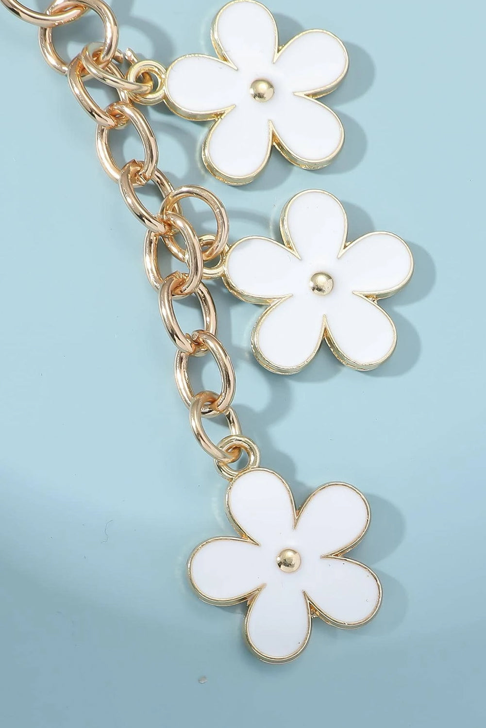 Gold chain bracelet with white flower charms on a light blue background