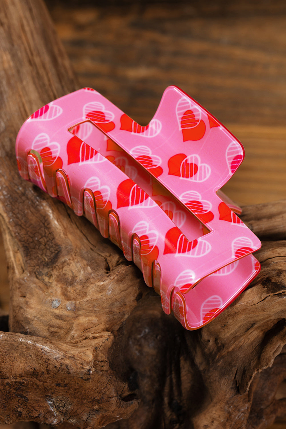Pink hair clip with red heart pattern on a wooden surface