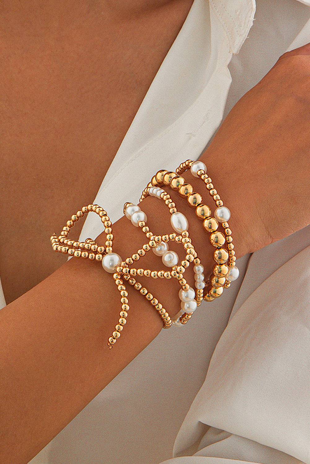 Gold and pearl beaded bracelets on a wrist with a neutral background