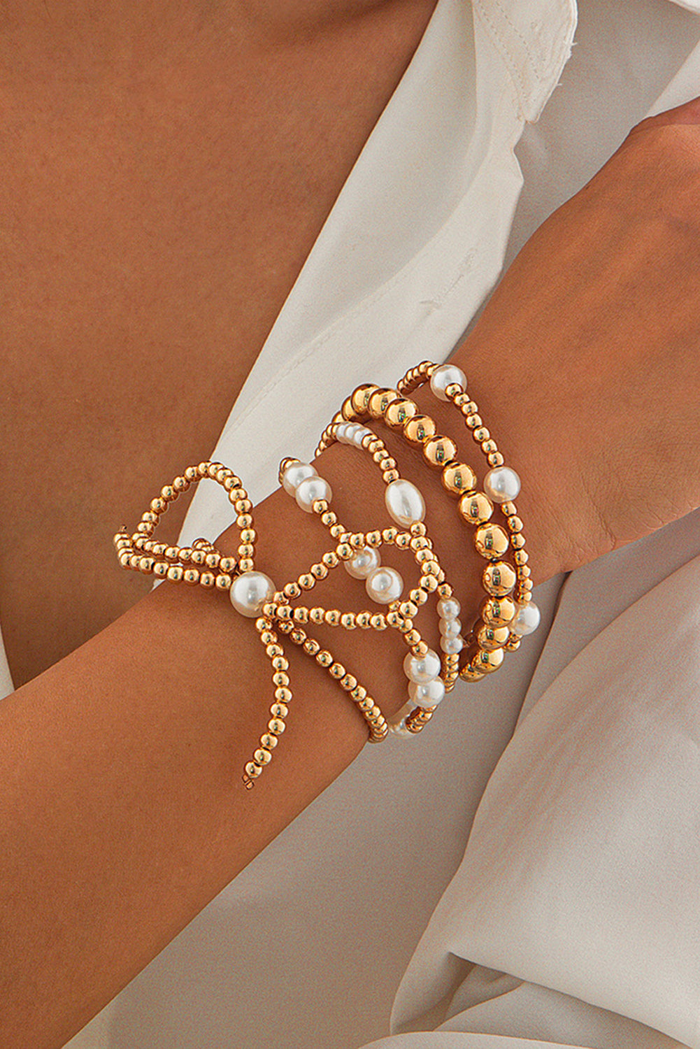 Gold and pearl beaded bracelets on a wrist with a neutral background