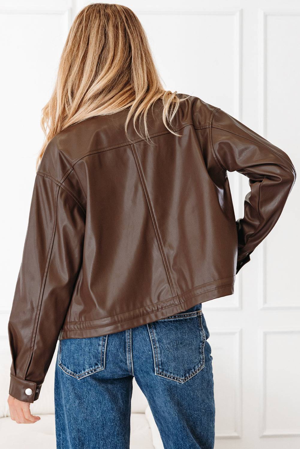 Person wearing a brown leather jacket and blue jeans against a white background