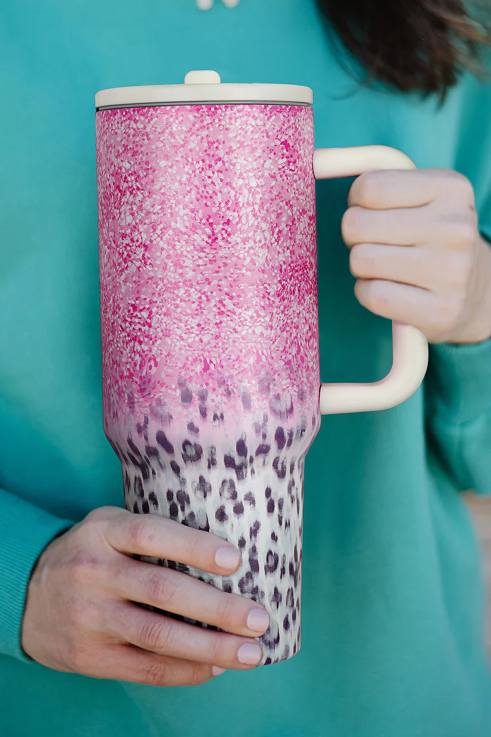 Person holding a pink and leopard print tumbler against a teal background