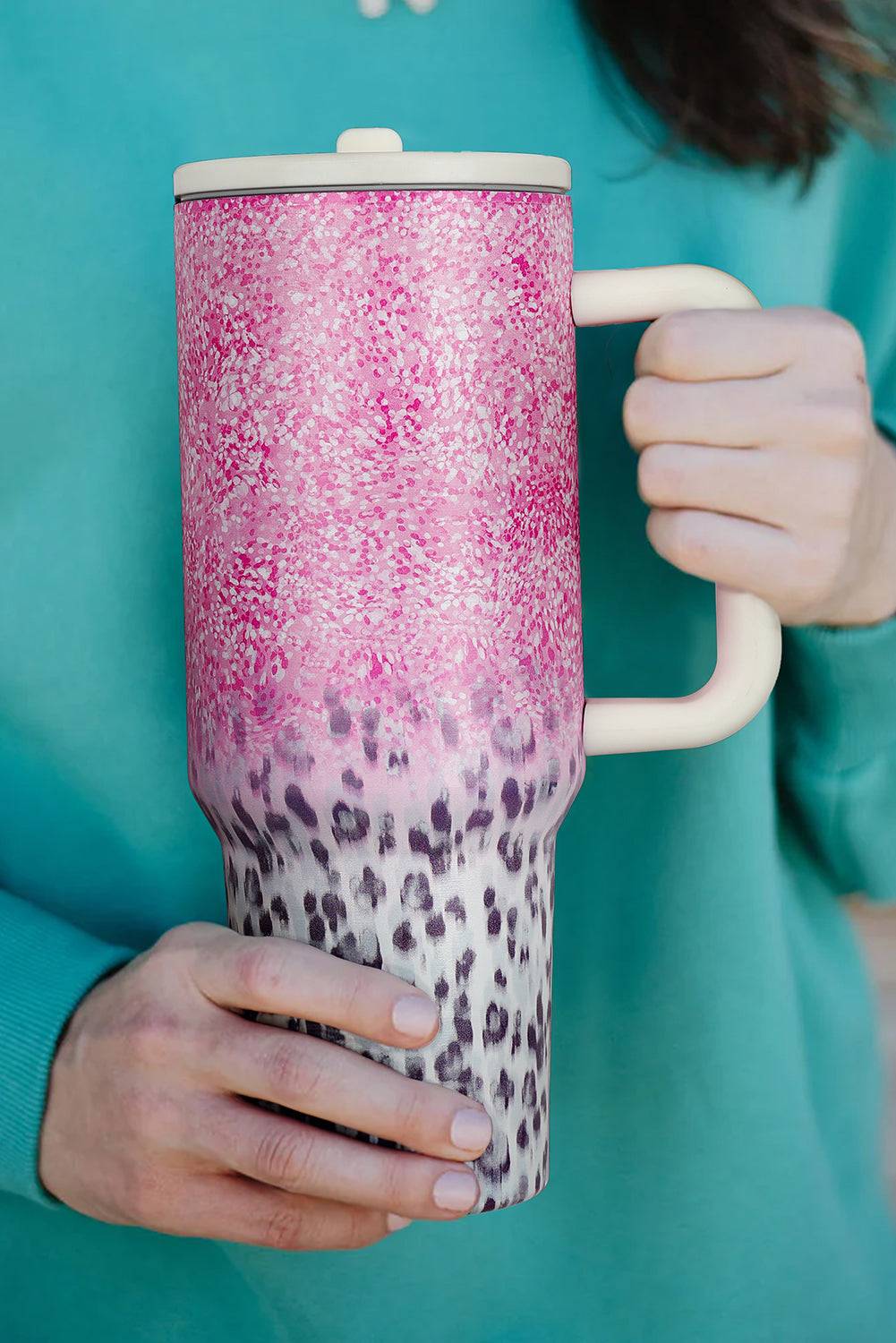 Person holding a pink and leopard print tumbler against a teal background
