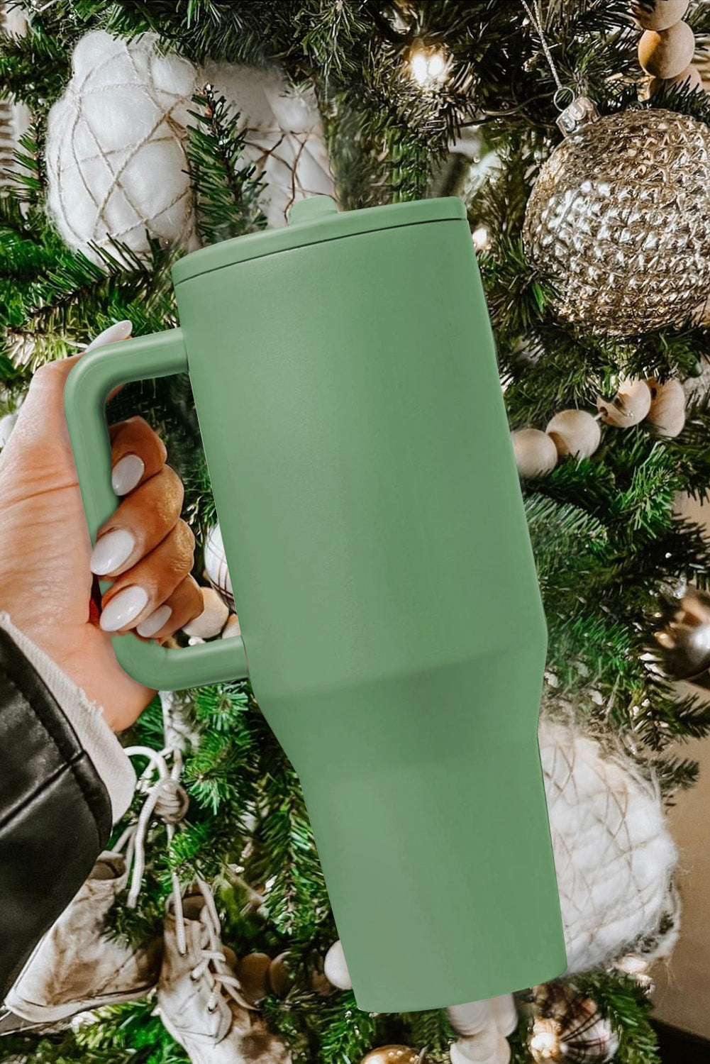 Green tumbler held in front of a decorated Christmas tree