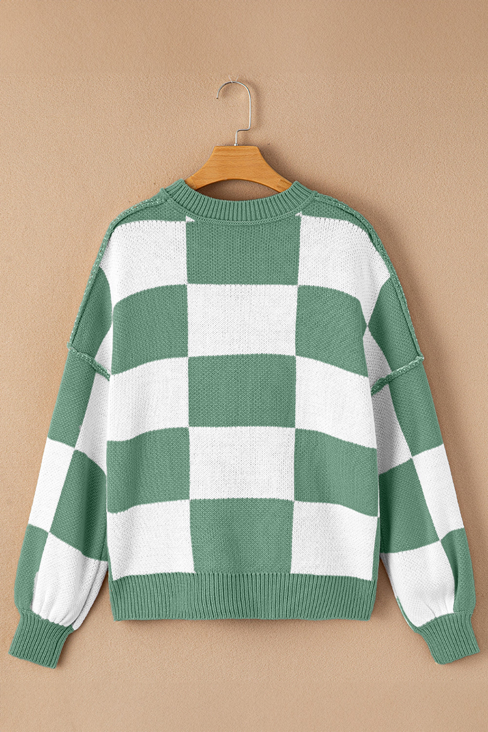 Green and white checkered sweater on a wooden hanger against a beige background