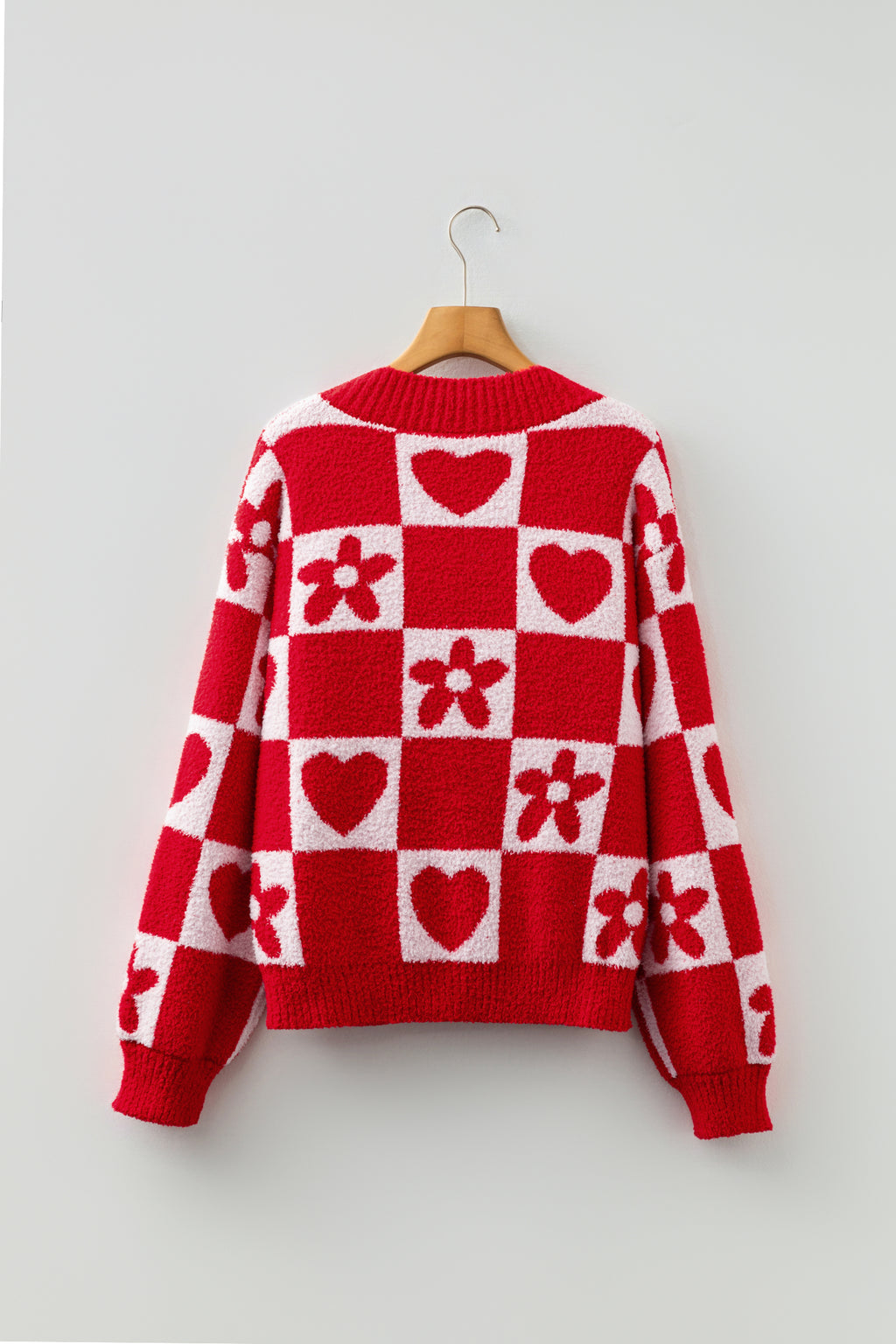 Red and white checkered sweater with heart and flower patterns on a hanger against a light gray background