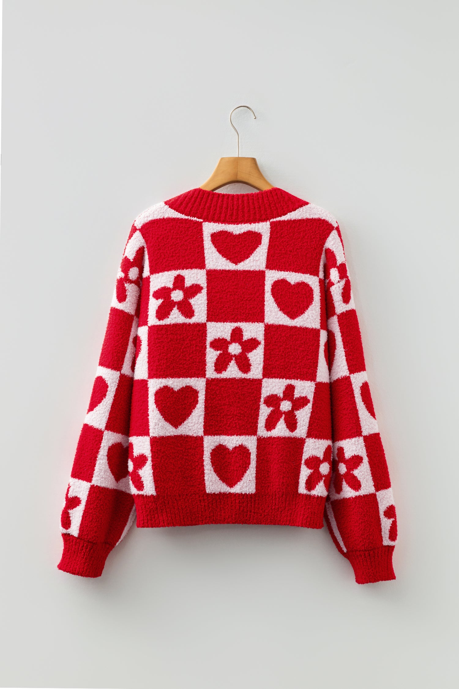 Red and white checkered sweater with heart and flower patterns on a hanger against a light gray background