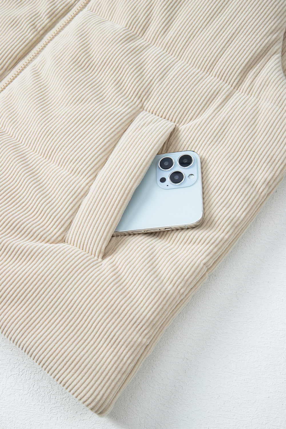 Phone in a pocket of a beige corduroy jacket on a light background