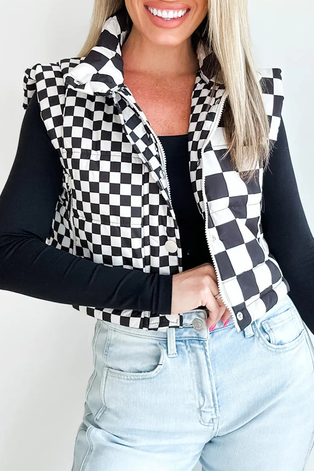 Person wearing a black and white checkered vest over a black long-sleeve top and light blue jeans.