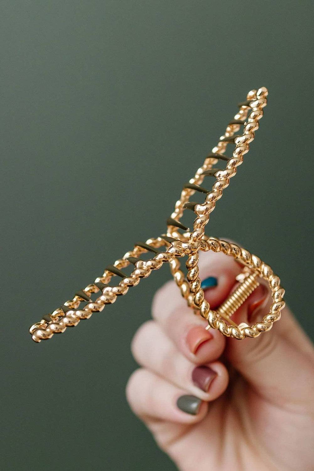 Gold chain hair clip held by a hand against a green background