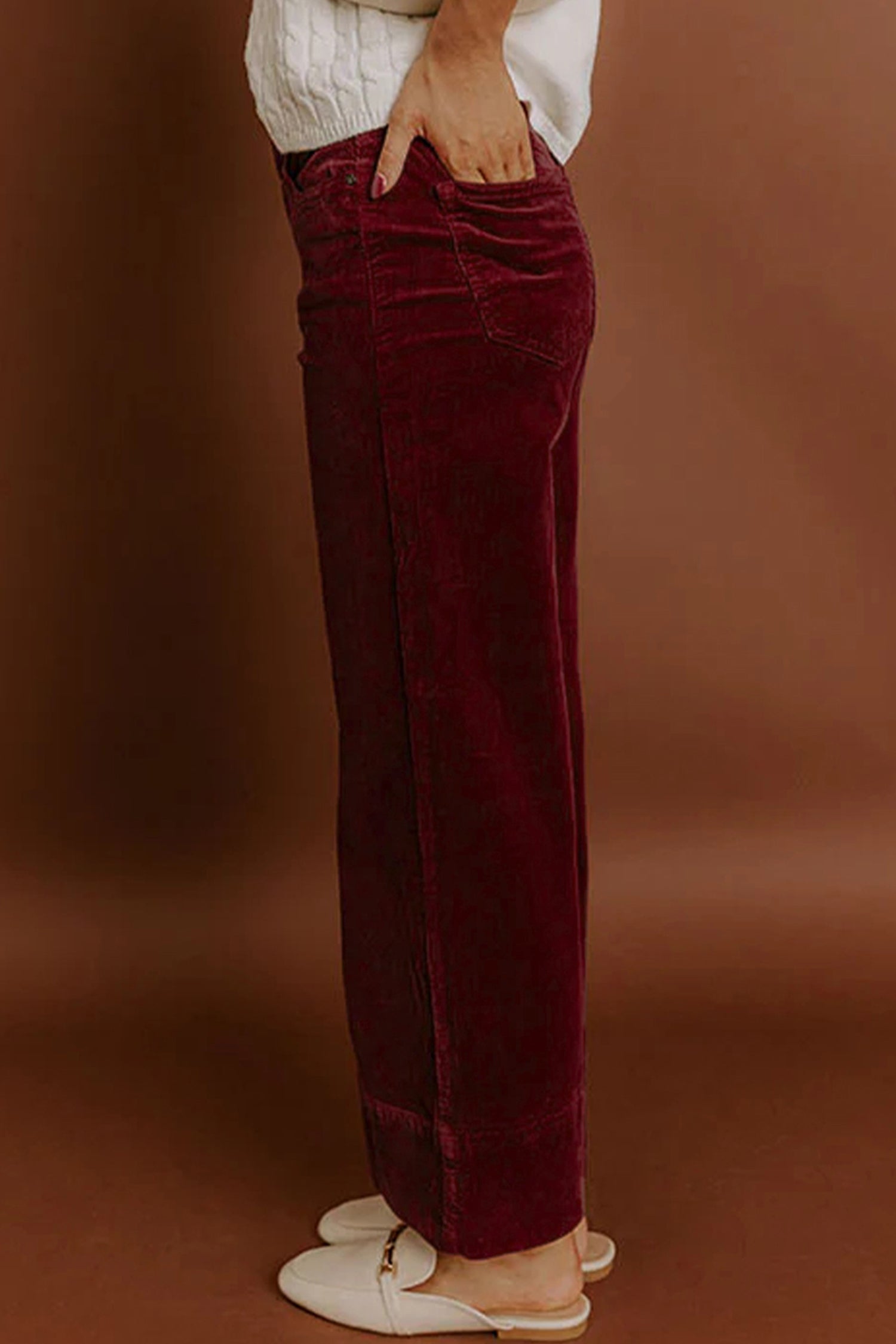 Maroon velvet pants worn by a person on a brown background