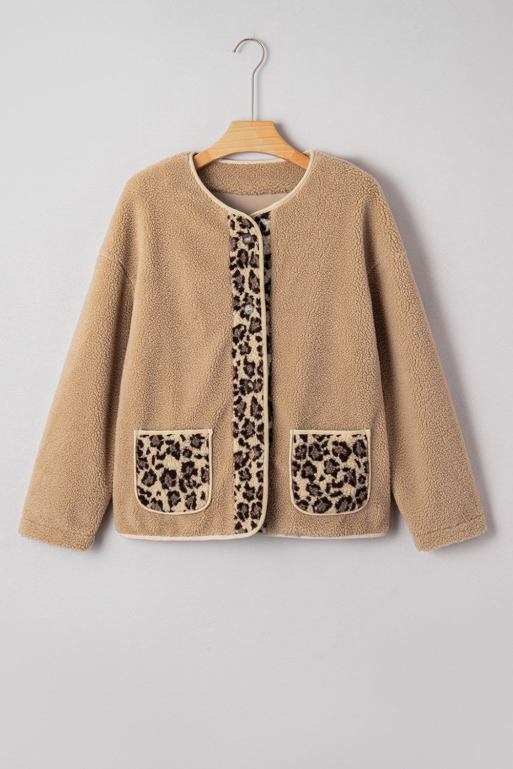 Beige cardigan with leopard print pockets on a hanger against a gray background