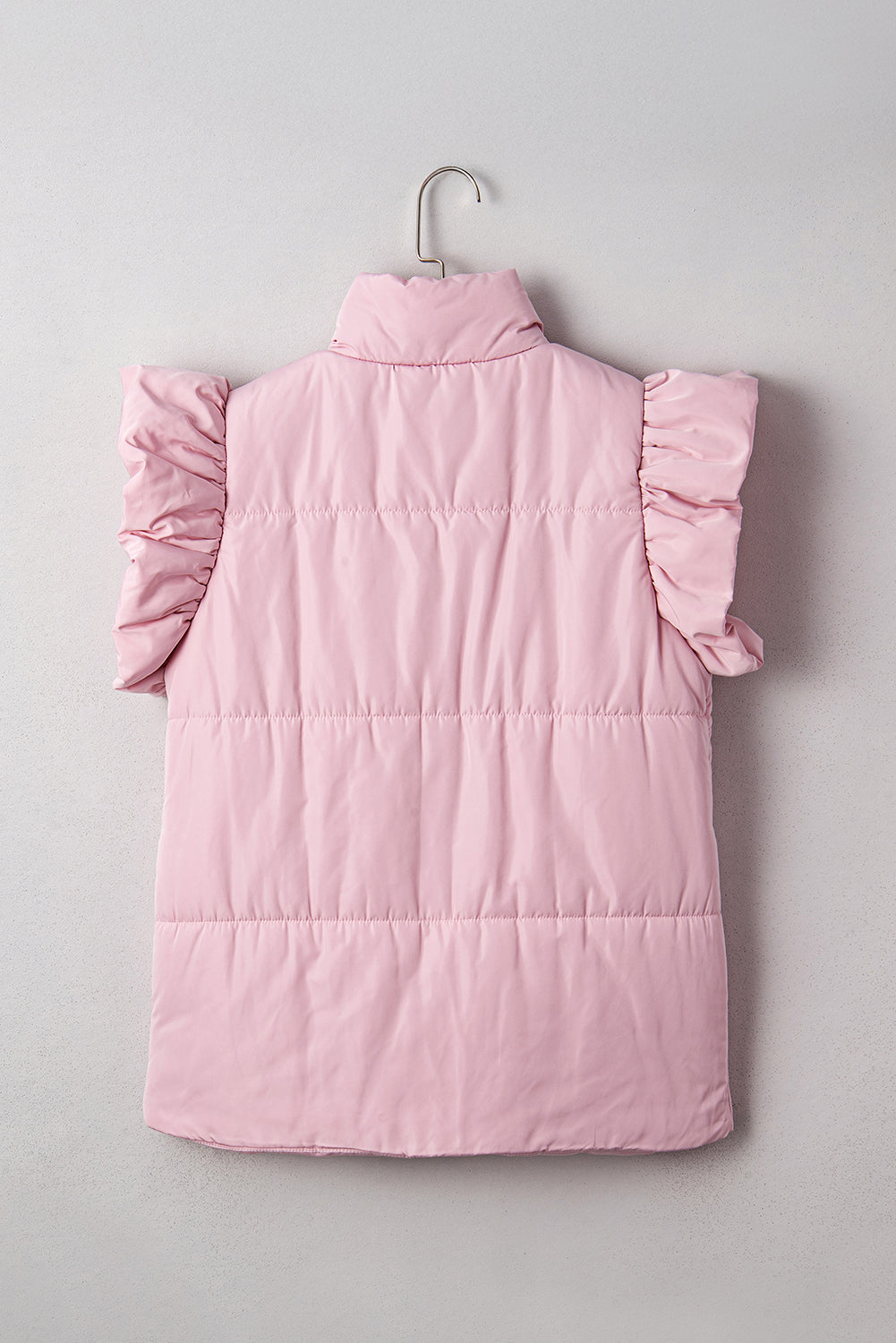 Pink puffer vest with ruffled shoulders on a hanger against a light gray background
