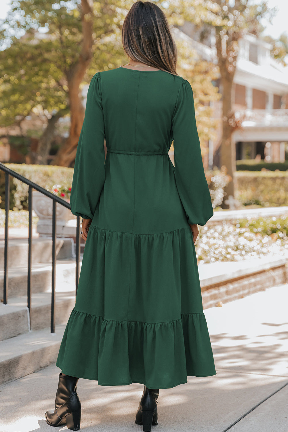 Woman wearing a green dress with long sleeves and ruffled layers, standing outdoors.
