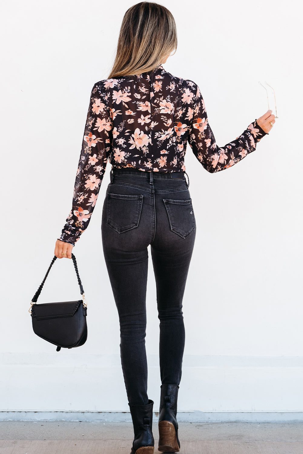 Woman wearing a floral blouse and black jeans with a black handbag against a white background