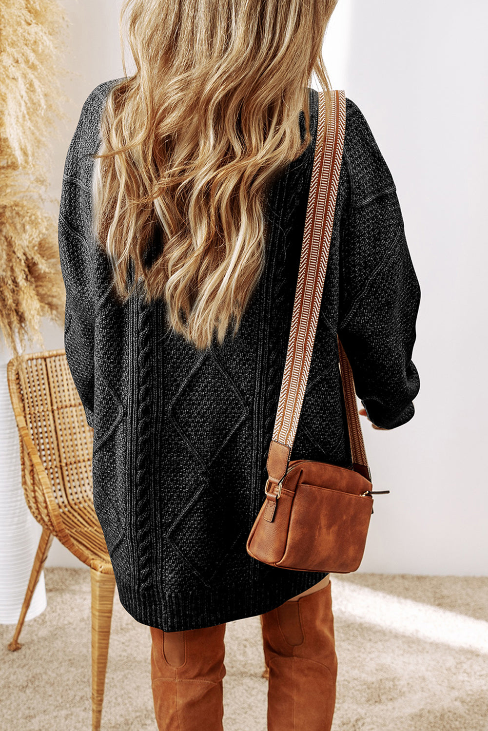 Person wearing a black cable knit sweater and brown leather boots with a brown leather bag.