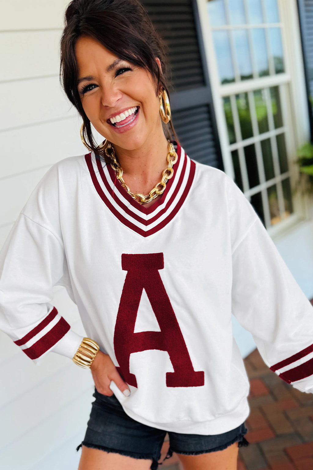 Woman wearing a white sweater with a red 'A' logo, smiling outdoors.