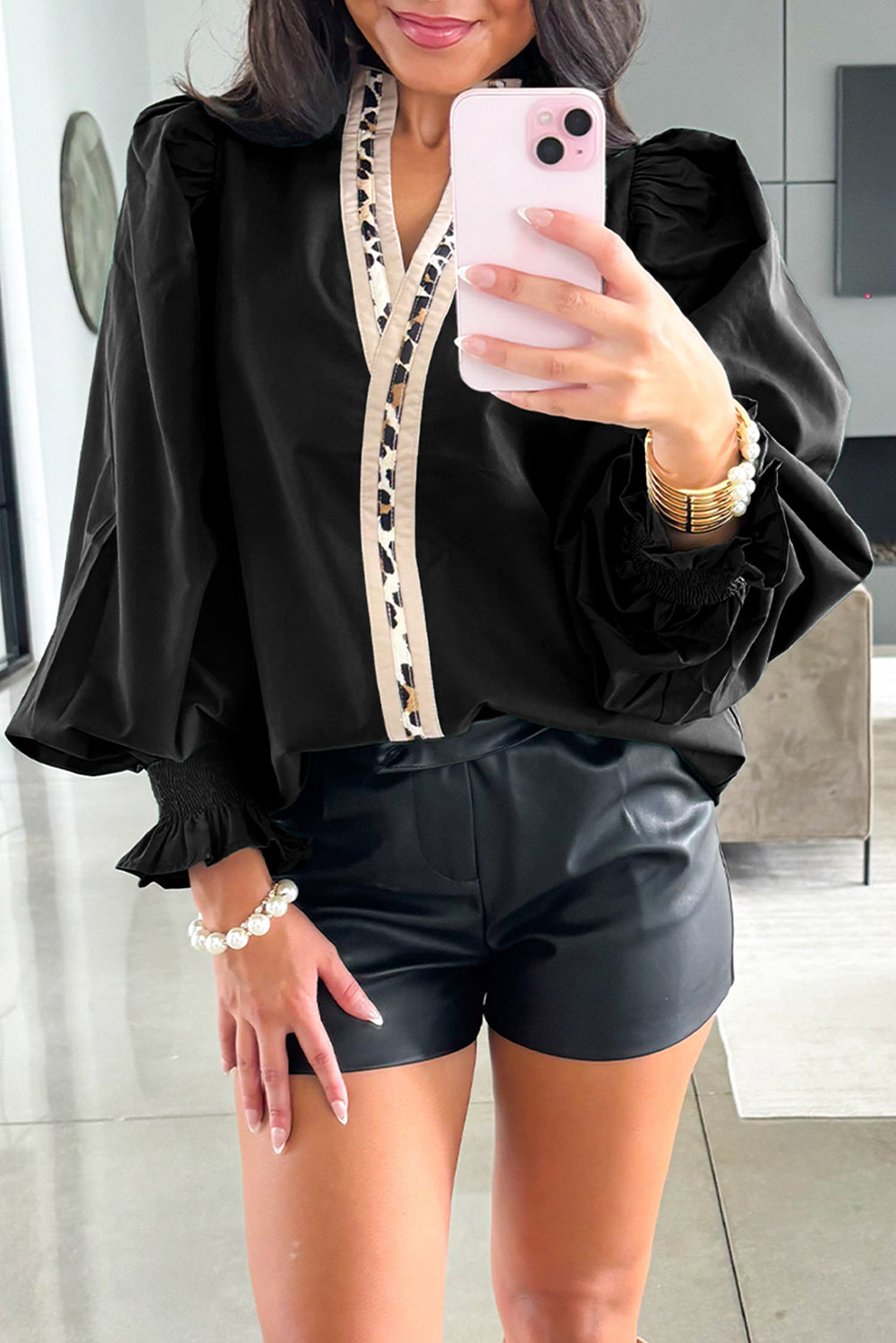 Person wearing a black blouse with ruffled sleeves and leopard print trim, taking a mirror selfie.