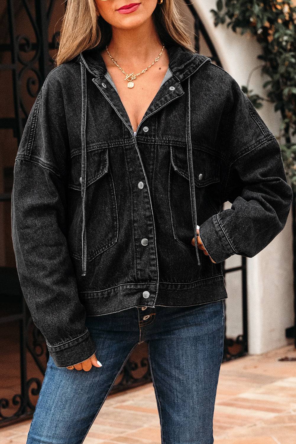 Person wearing a black denim jacket and blue jeans outdoors.