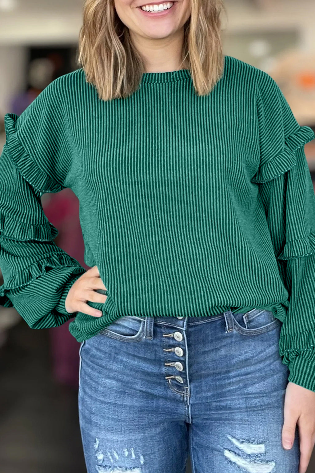 Person wearing a green ribbed sweater with ruffled sleeves and blue jeans.