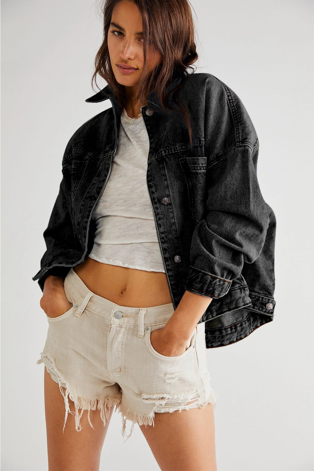 Woman wearing a black denim jacket, gray t-shirt, and light denim shorts on a white background