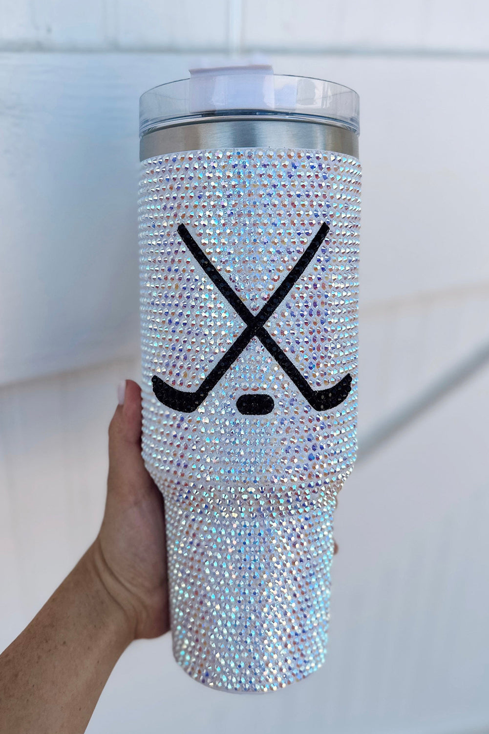 Silver blinged-out tumbler with hockey stick and puck design held by a hand against a white background