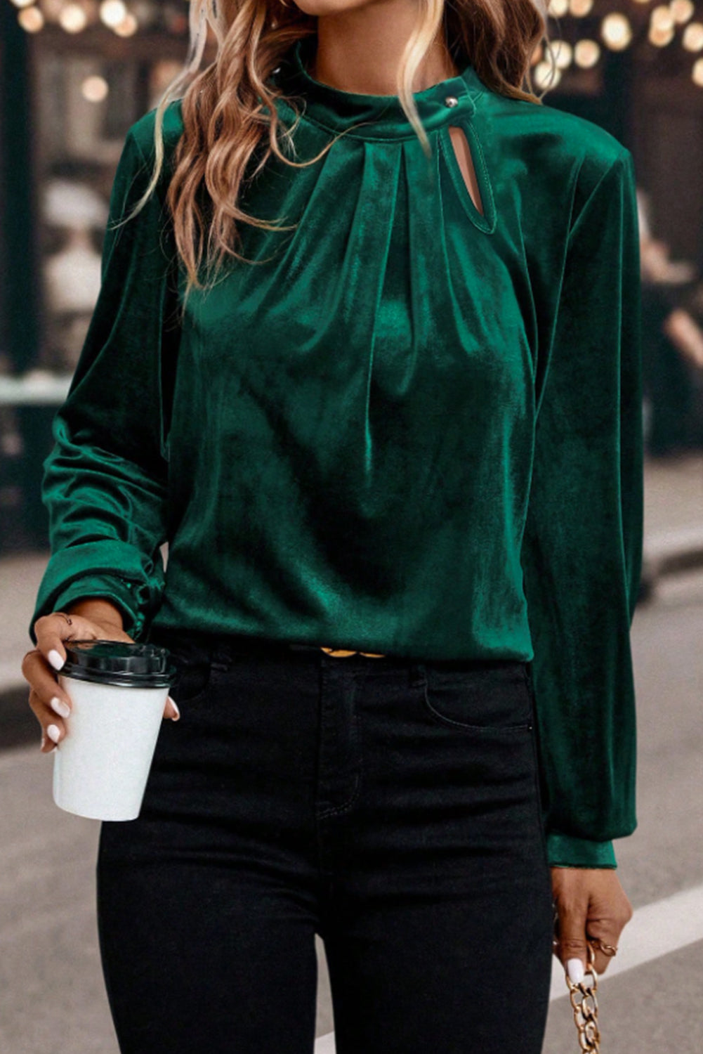 Person wearing a green blouse with cut-out details and holding a coffee cup.