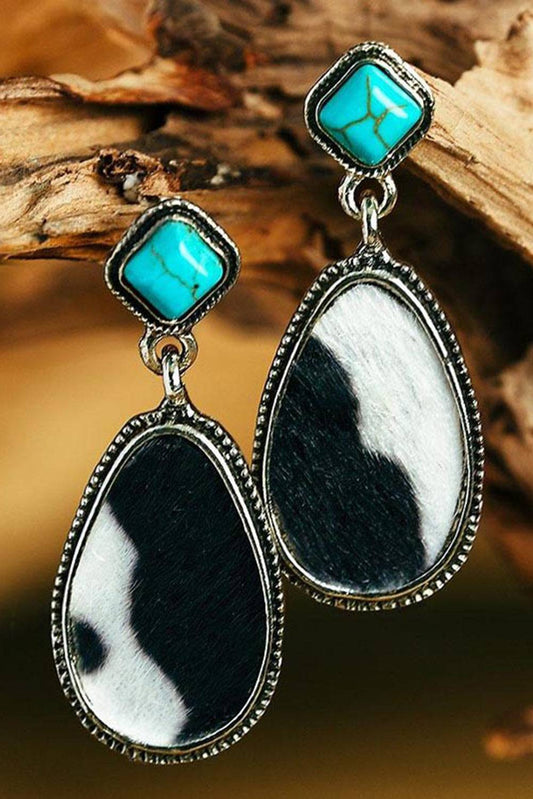 Pair of earrings with turquoise and black and white stones on a wooden background
