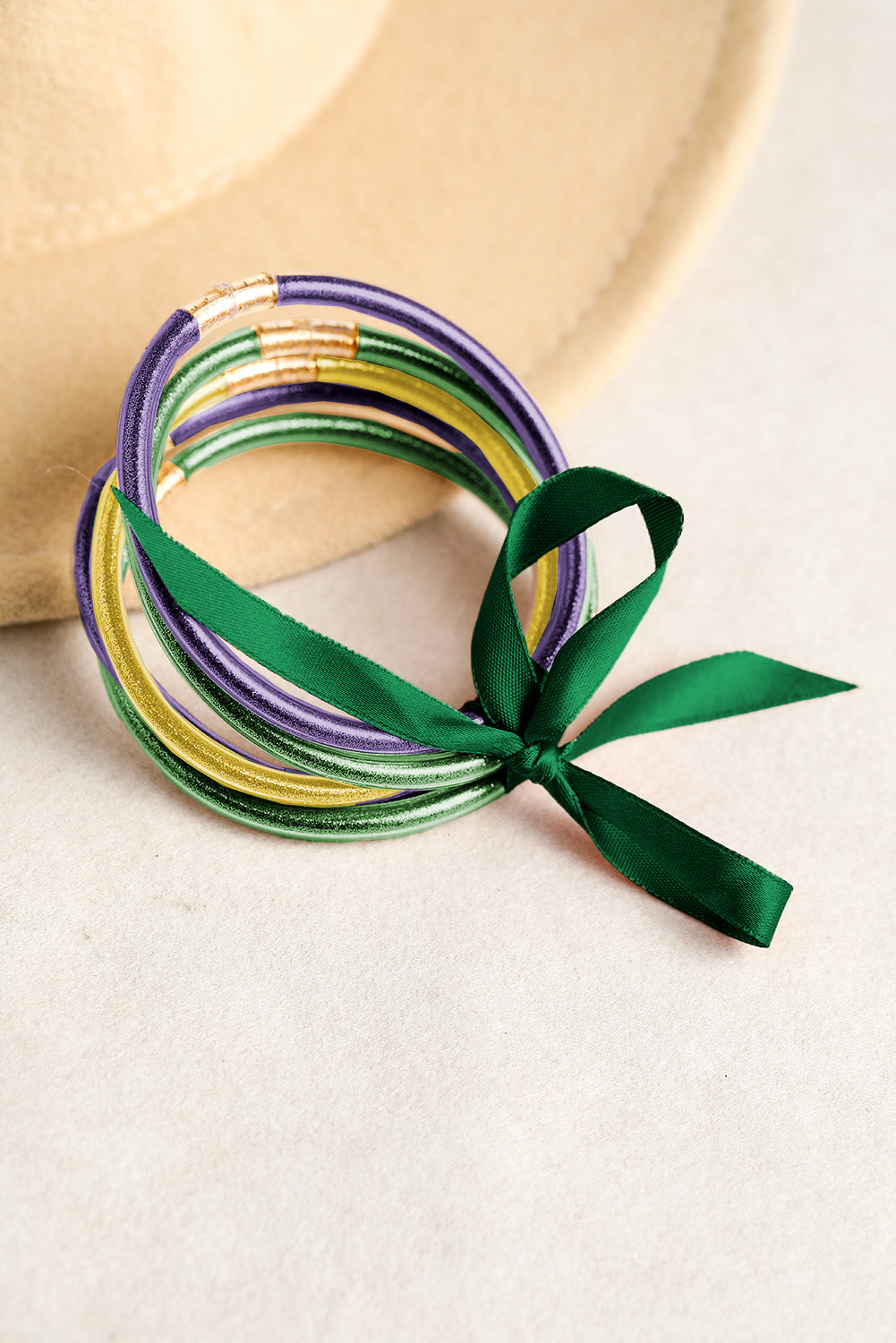 Set of colorful bracelets with a green ribbon on a beige background