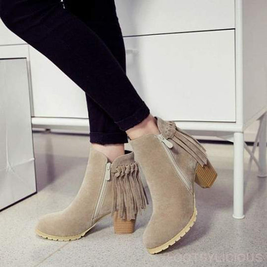Beige ankle boots with fringes worn by a person on a light gray floor.
