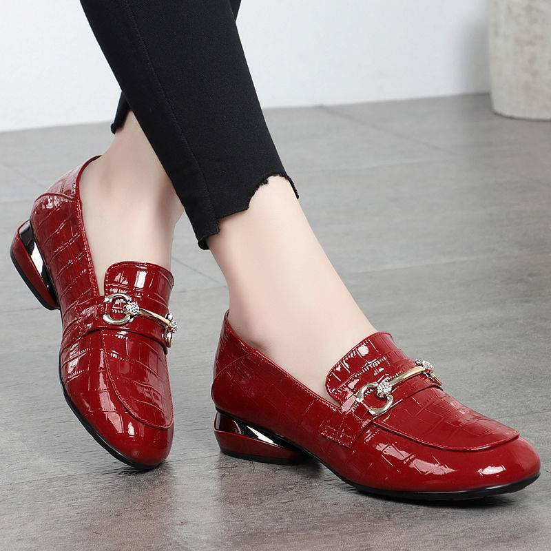 Red patent leather shoes with gold buckles worn by a person on a gray floor.
