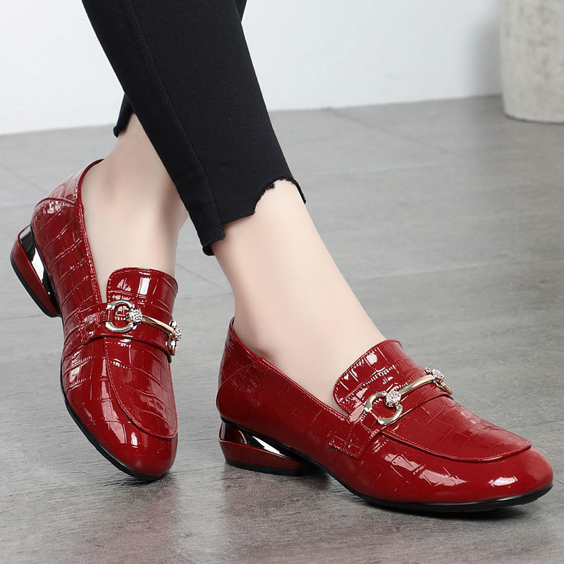 Red patent leather shoes with gold buckles worn by a person on a gray floor.