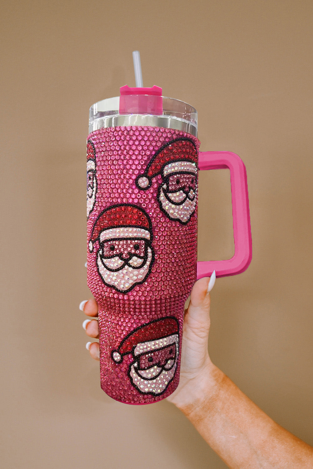 Pink blinged-out tumbler with Santa hats held by a hand against a beige background